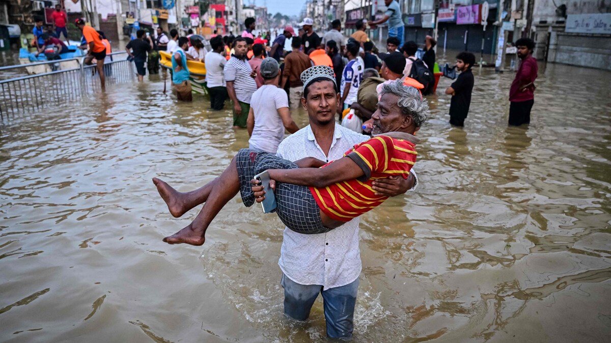TOPSHOT - A youth carries an elderly man as they wade through a flooded street after heavy rainfall in Wellampitiya on the outskirts of Colombo on November 30, 2025. The death toll from floods and landslides triggered by Cyclone Ditwah has risen to at least 334 people across Sri Lanka, with nearly 400 still missing, the Disaster Management Centre said on November 30. (Photo by Ishara S. KODIKARA / AFP)