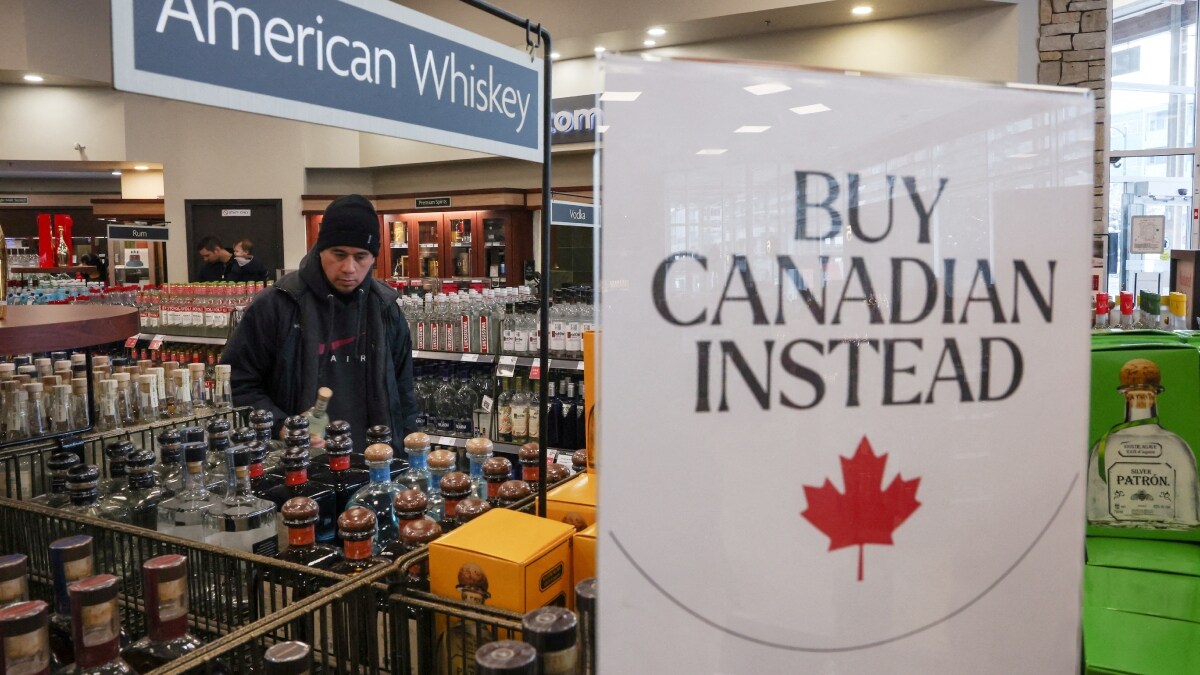 A customer holds a bottle as a sign that reads ''Buy Canadian Instead'' is displayed after the top five U.S. liquor brands were removed from sale at B.C. Liquor Stores in Vancouver, British Columbia | Reuters 