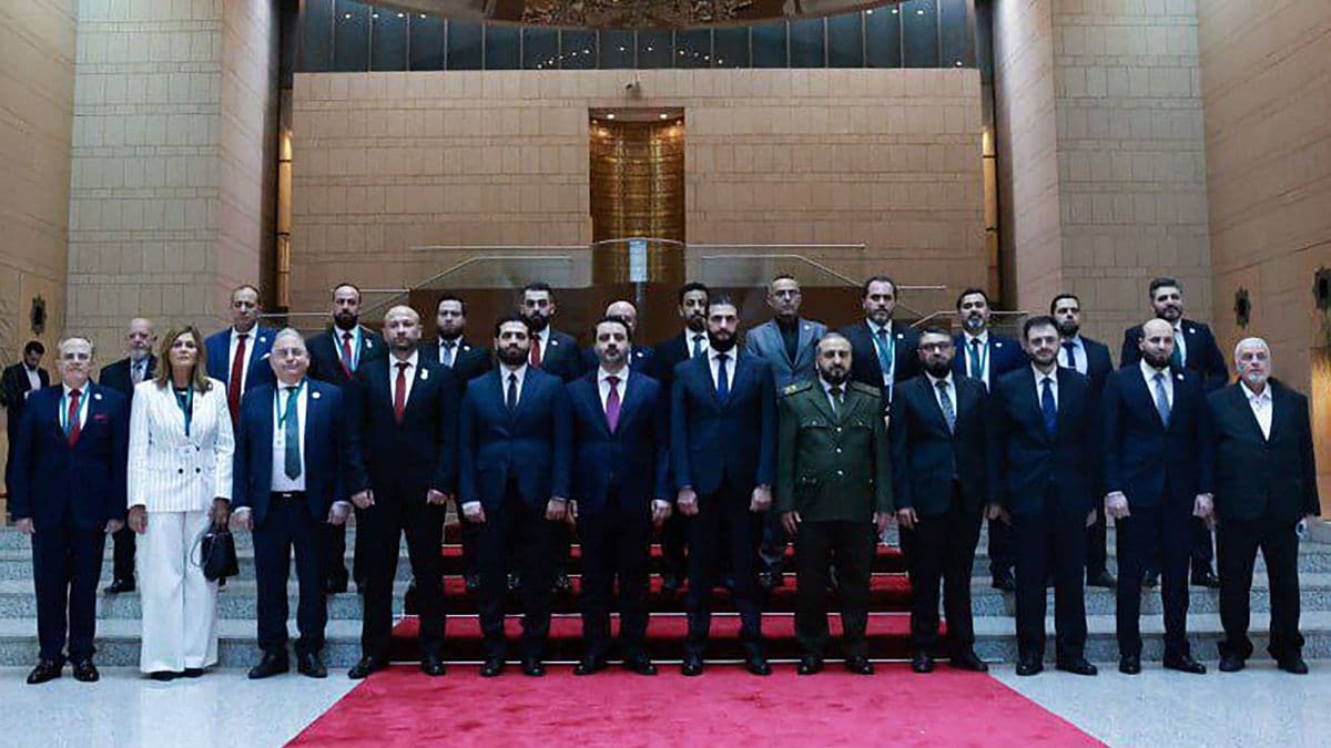 A handout picture released by the official Syrian Arab News Agency (SANA) on March 30, 2025, shows Syria's interim President Ahmed al-Sharaa (6th-R) and Foreign Minister Asaad al-Shibani (6th-L) posing for a picture with the new transitional government in Damascus | AFP