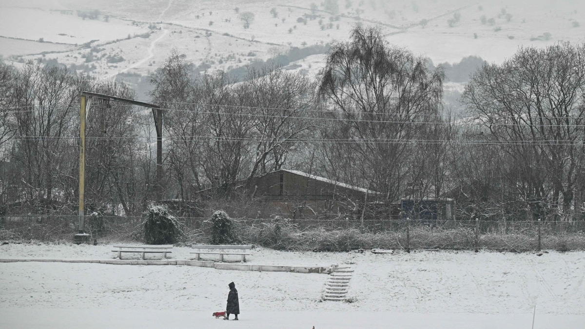 A pedestrian walks their dog across a snow-covered cricket pitch in the town of Glossop, Derbyshire | AFP