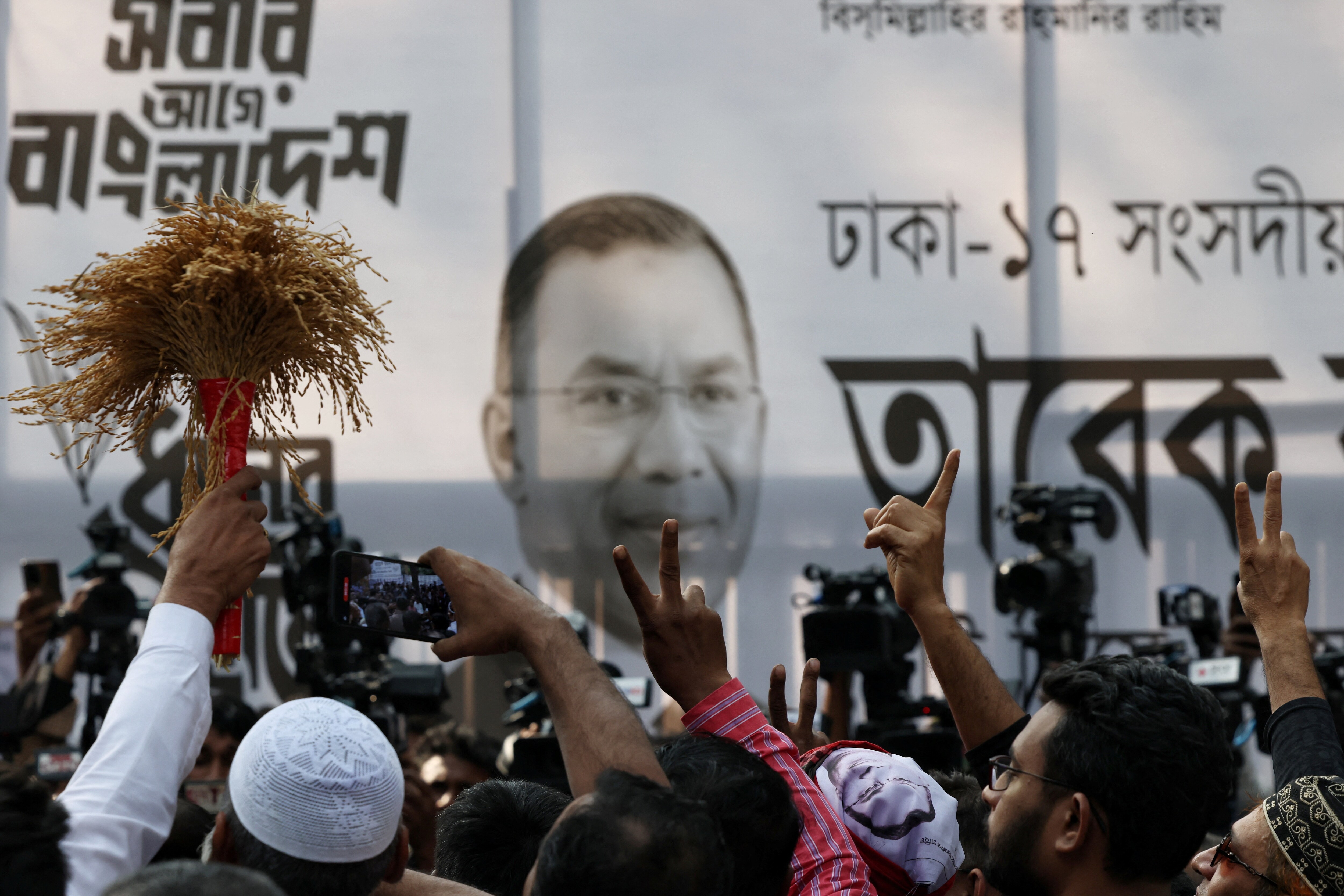 Supporters of the Bangladesh Nationalist Party (BNP) show a victory sign in front of a banner with Tarique Rahman’s photo, as the results project BNP's victory in the 13th general election, in Dhaka, Bangladesh | Reuters
